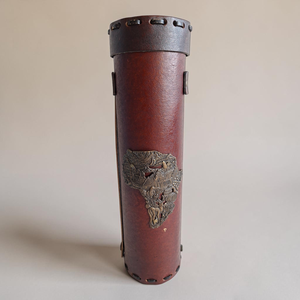 Leren flessenkoker met een messing reliëf in de vorm van de kaart van Afrika, met daarin een gedetailleerd tafereel.
