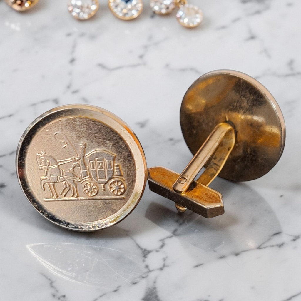 Vintage ronde goudkleurige manchetknopen met gedetailleerd reliëf van een klassieke postkoets, diameter 22 mm.
