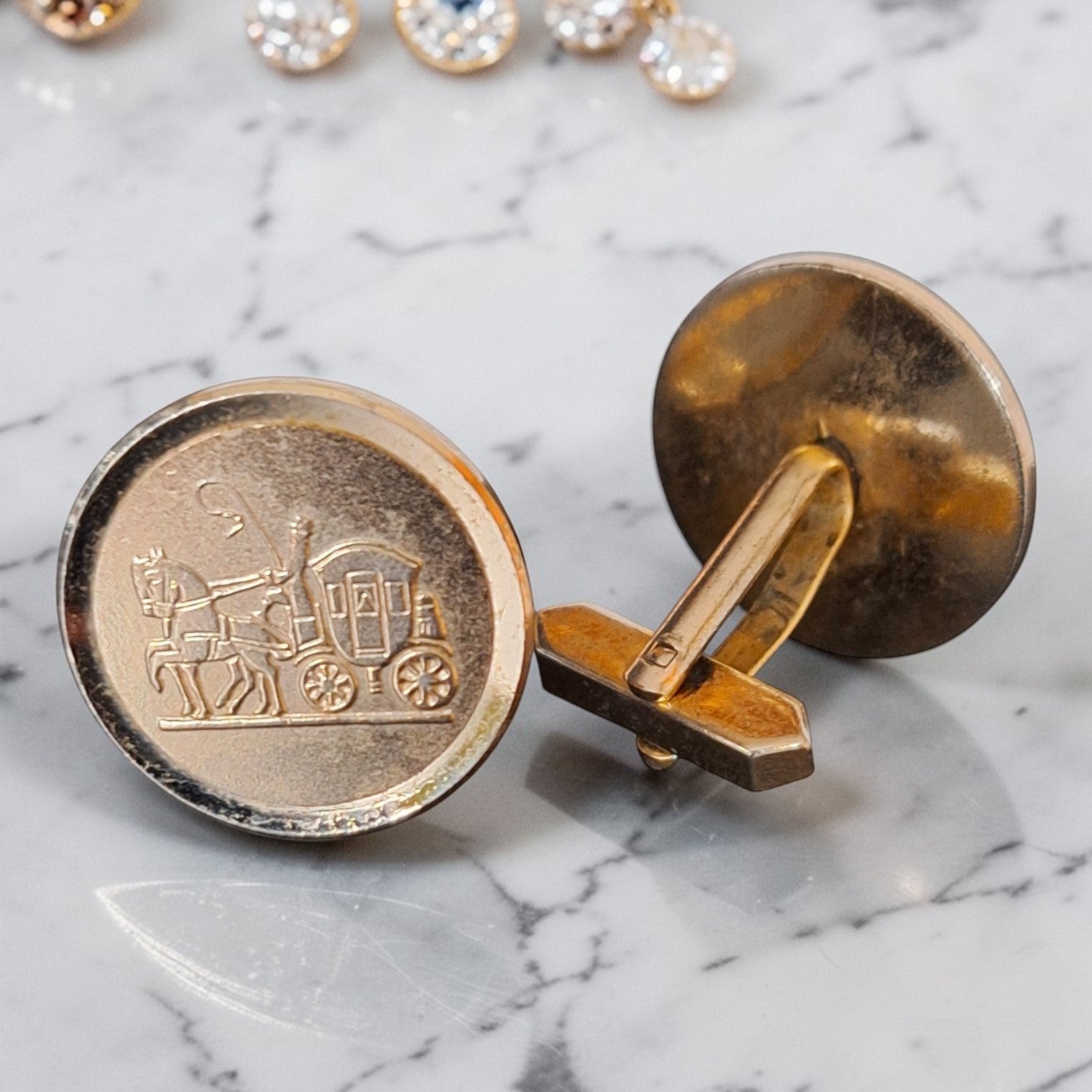 Vintage ronde goudkleurige manchetknopen met gedetailleerd reliëf van een klassieke postkoets, diameter 22 mm.
