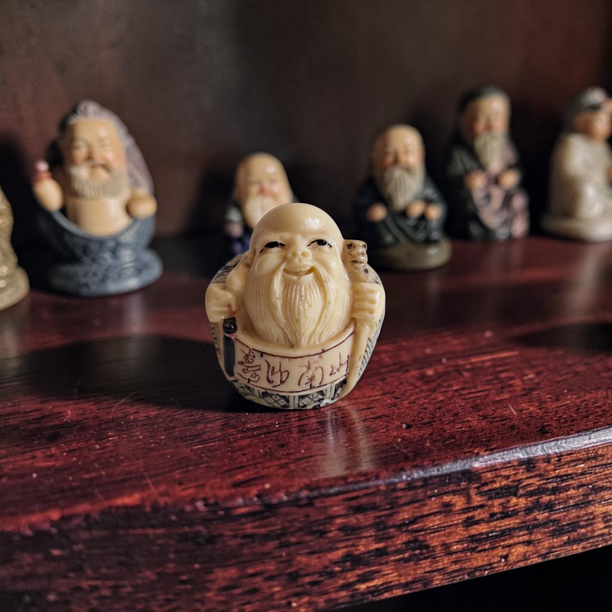 Miniatuur netsuke-stijl beeldje van een lachende wijsgeer met kaal hoofd, lange baard en kalligrafie op het ivoorkleurige gewaad.