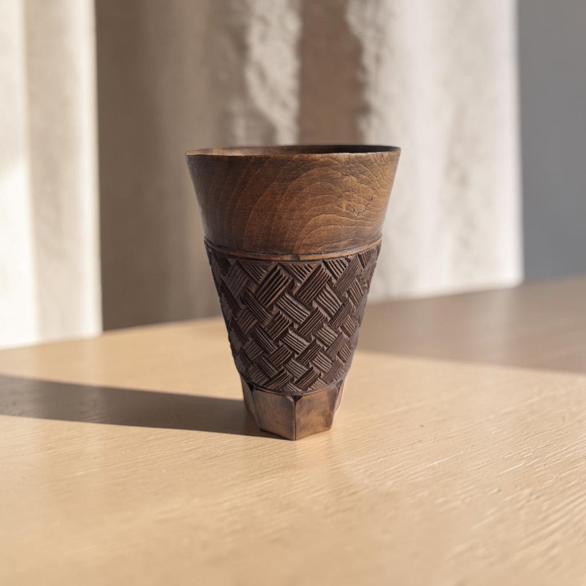 Handgesneden Kuba palmwijnbeker van warmbruin hardhout met geometrisch vlechtwerk in hoogreliëf, een gladde bovenrand en een achthoekige voet.
