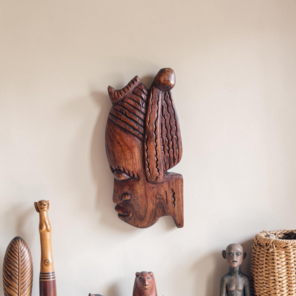 Handgesneden houten wanddecoratie van een gestileerd vrouwenhoofd in profiel met uitgesneden lineaire patronen en een gedetailleerd haardecor.
