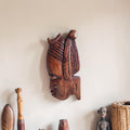 Handgesneden houten wanddecoratie van een gestileerd vrouwenhoofd in profiel met uitgesneden lineaire patronen en een gedetailleerd haardecor.
