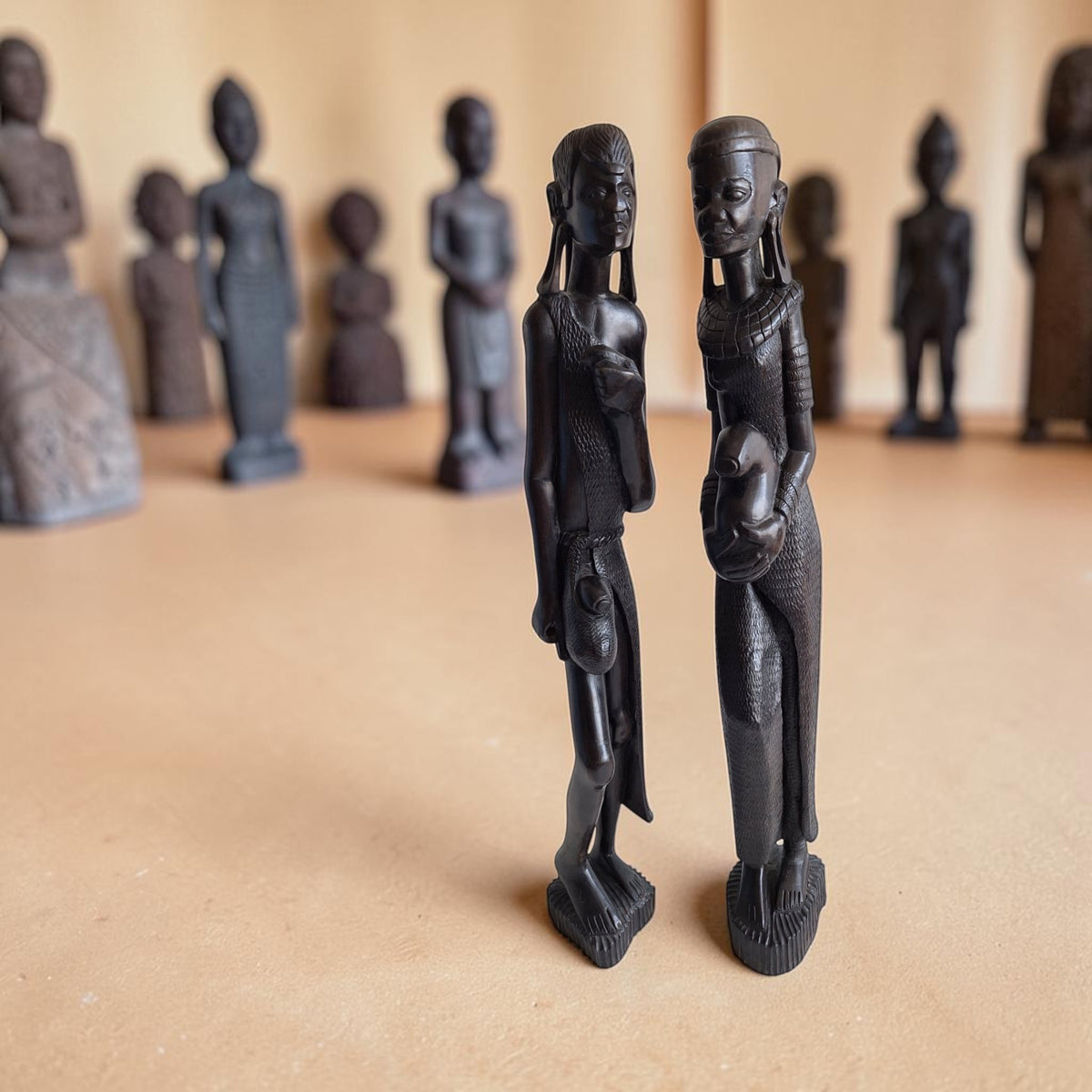 Paar handgesneden houten Maasai-figuren in traditionele kleding, met een man zonder speren en een vrouw die een waterpot vasthoudt.
