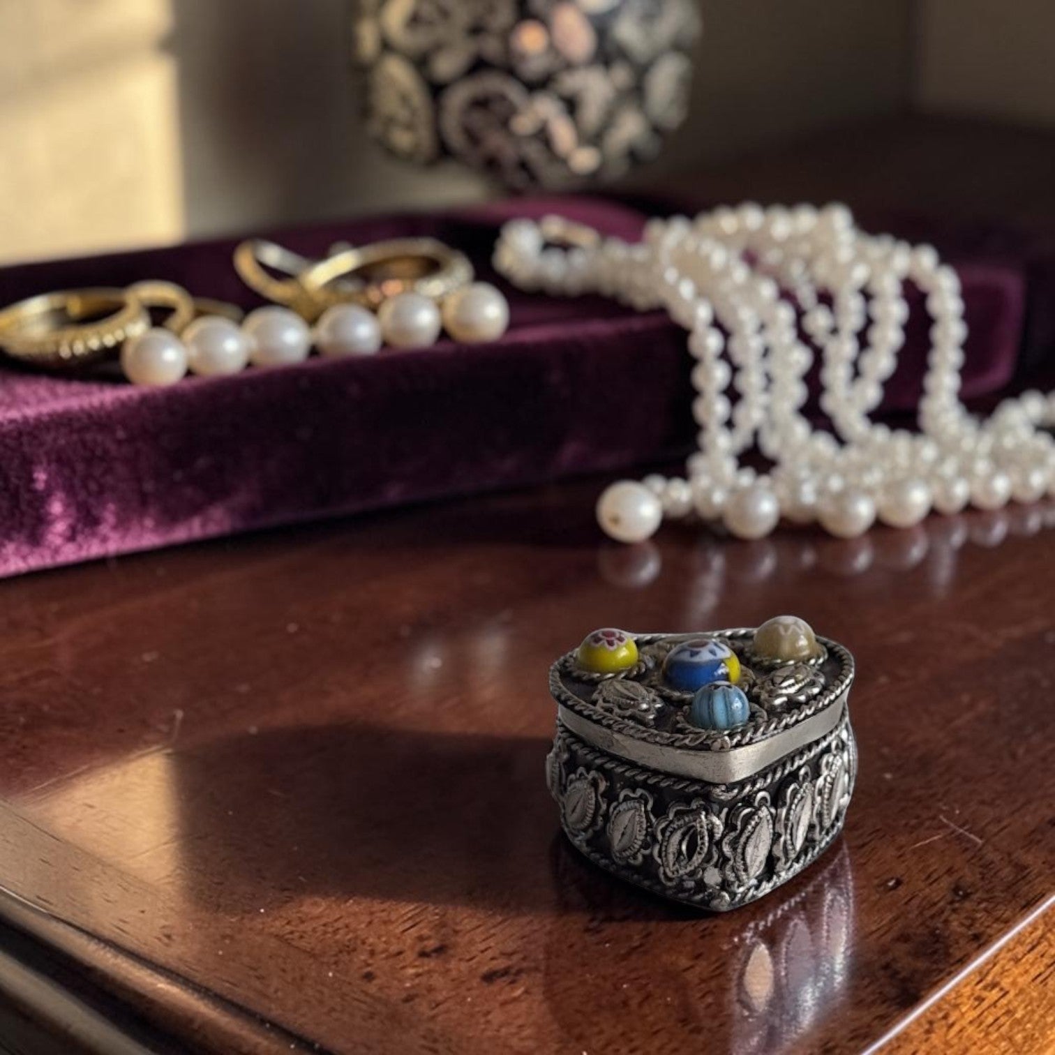 Hartvormig verzilverd pillendoosje met kleurrijke millefiori-glaskralen op het deksel in Murano-stijl, met fijne reliëfpatronen op de zijkanten.