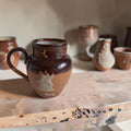 Bolle Royal Doulton Lambeth roomkan van donkerbruin en okerbeige steengoed met lichte oogstreliëfs en een gerestaureerd oor.