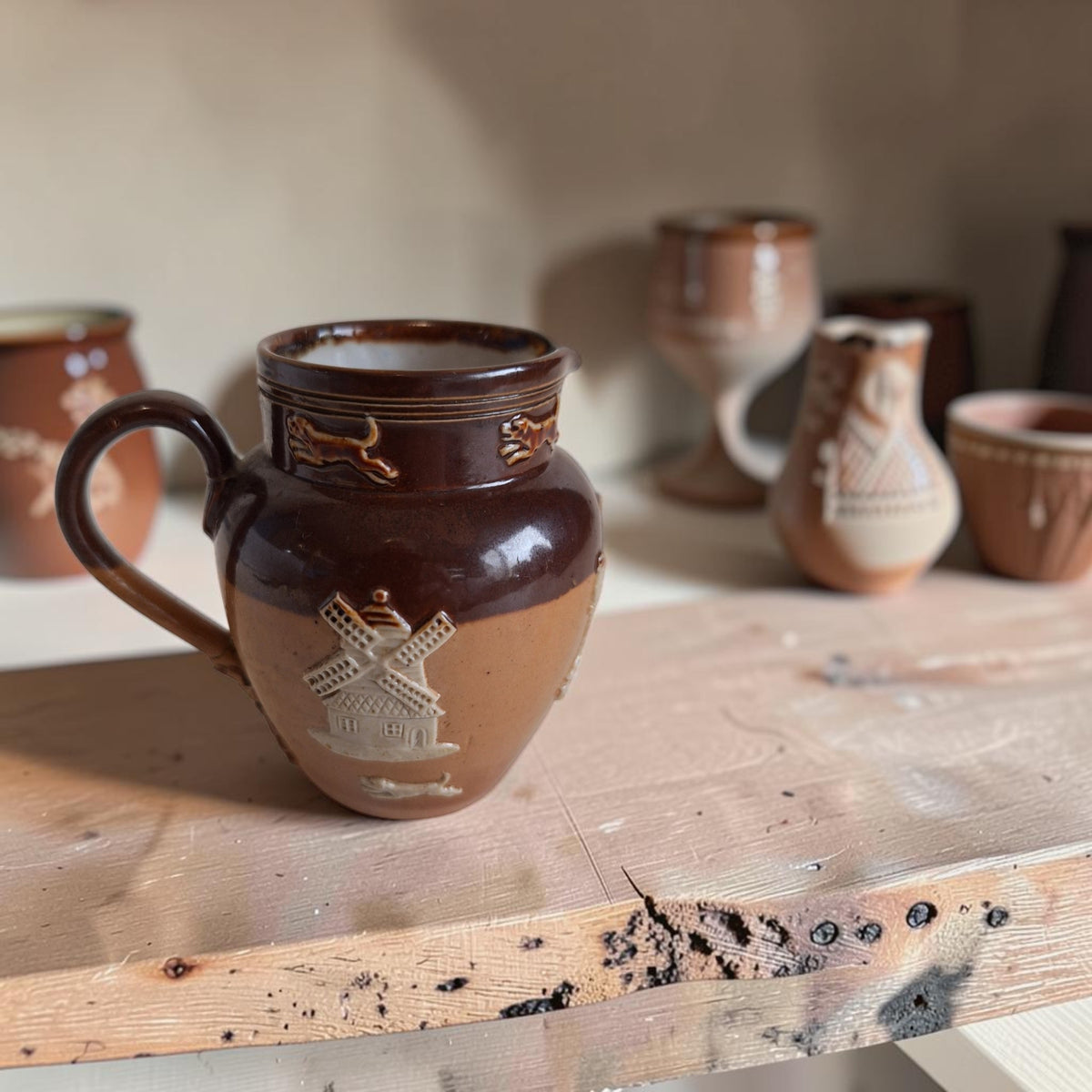Bolle Royal Doulton Lambeth roomkan van donkerbruin en okerbeige steengoed met lichte oogstreliëfs en een gerestaureerd oor.