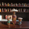 Set van drie handbeschilderde Japanse kokeshi poppetjes met traditionele hoedjes en kimono-details, hoogte groot 11 cm en klein ca. 5 cm.