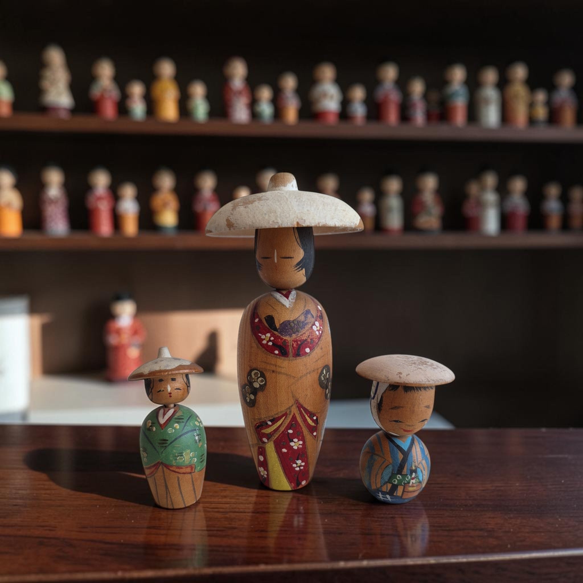 Set van drie handbeschilderde Japanse kokeshi poppetjes met traditionele hoedjes en kimono-details, hoogte groot 11 cm en klein ca. 5 cm.