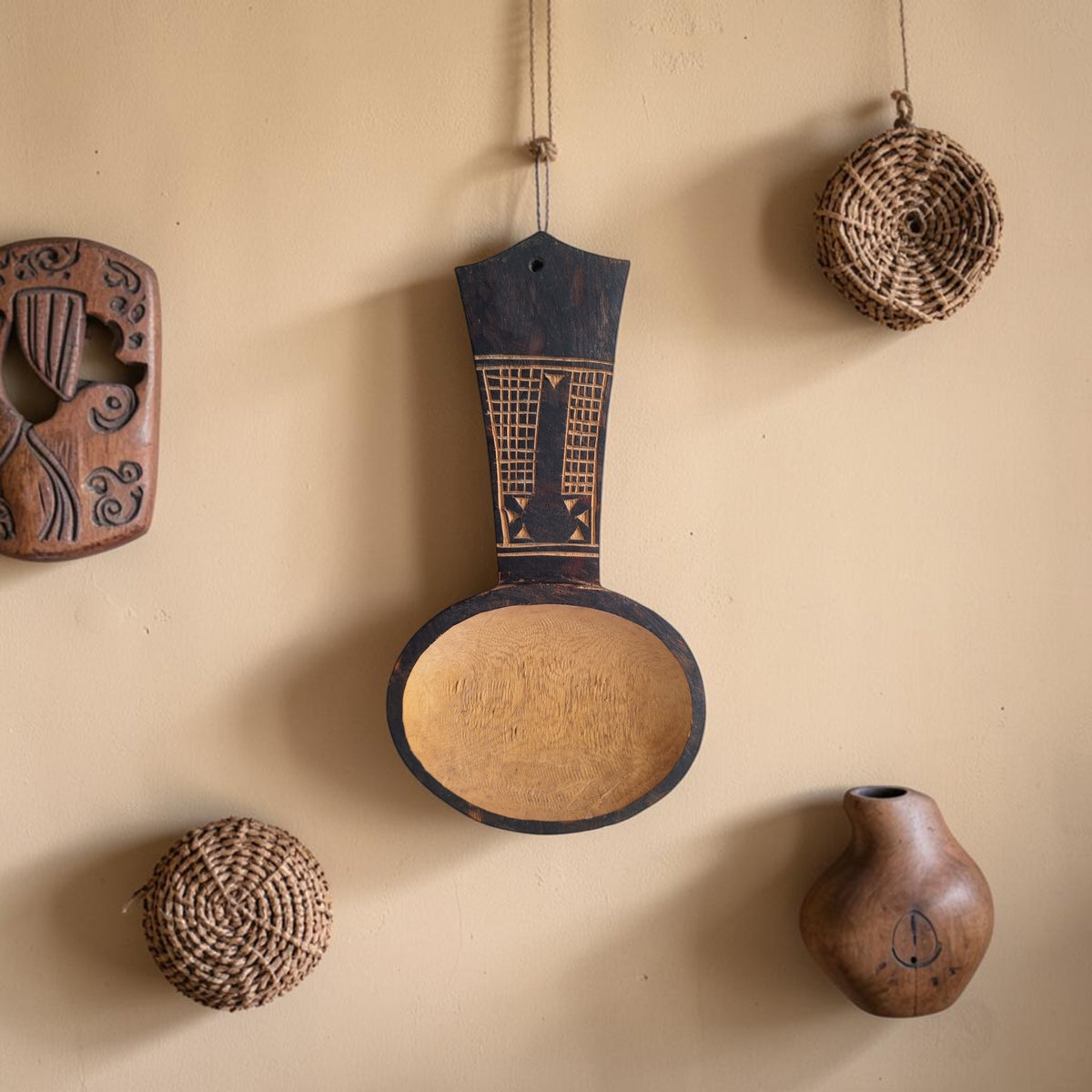 Handgemaakte houten lepel met brede ronde kom en donker handvat met ingegraveerde geometrische patronen en een ophangat.
