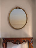 Vintage ovale wandspiegel met goudkleurige neoclassicistische lijst en strikornament aan de bovenzijde, 33 × 25,5 cm, Lodewijk XVI-stijl, 20e eeuw.