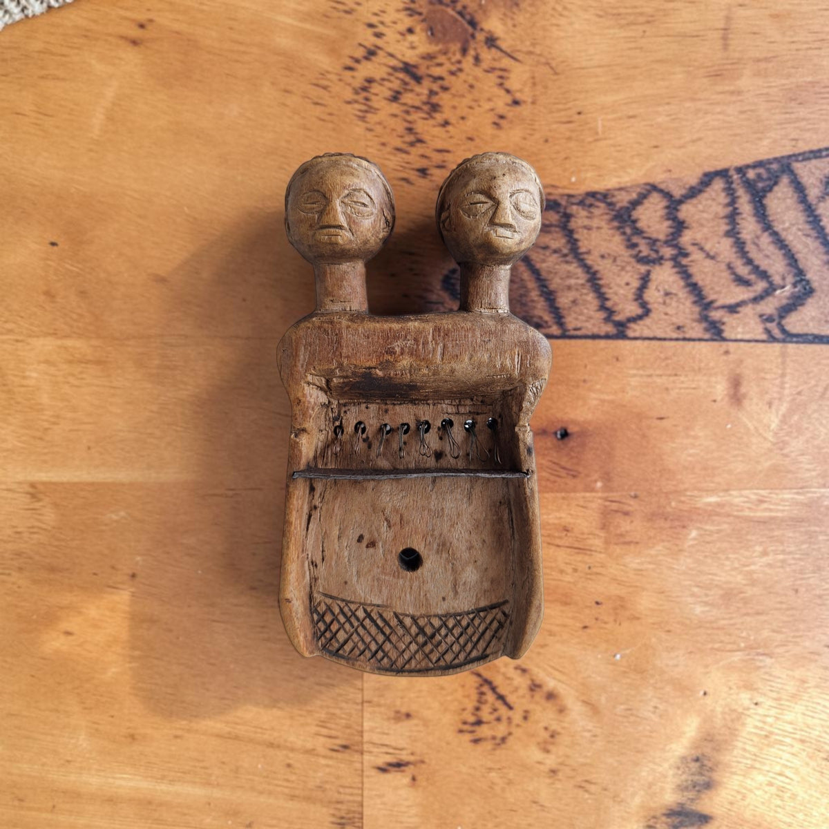 Houten sanza met twee gestileerde hoofden boven een klankkast met centraal klankgat, metalen klemmen en een ijzeren brug, zonder toetsen.
