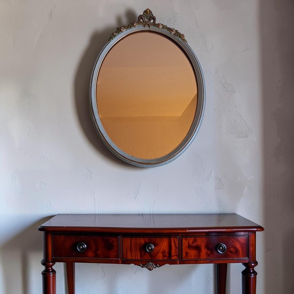 Vintage wandspiegel uit de jaren '70 met houten lijst, sierlijke bloemendetails, strikmotief aan de bovenzijde en oranje getint spiegelglas, 43 × 31,5 cm.
