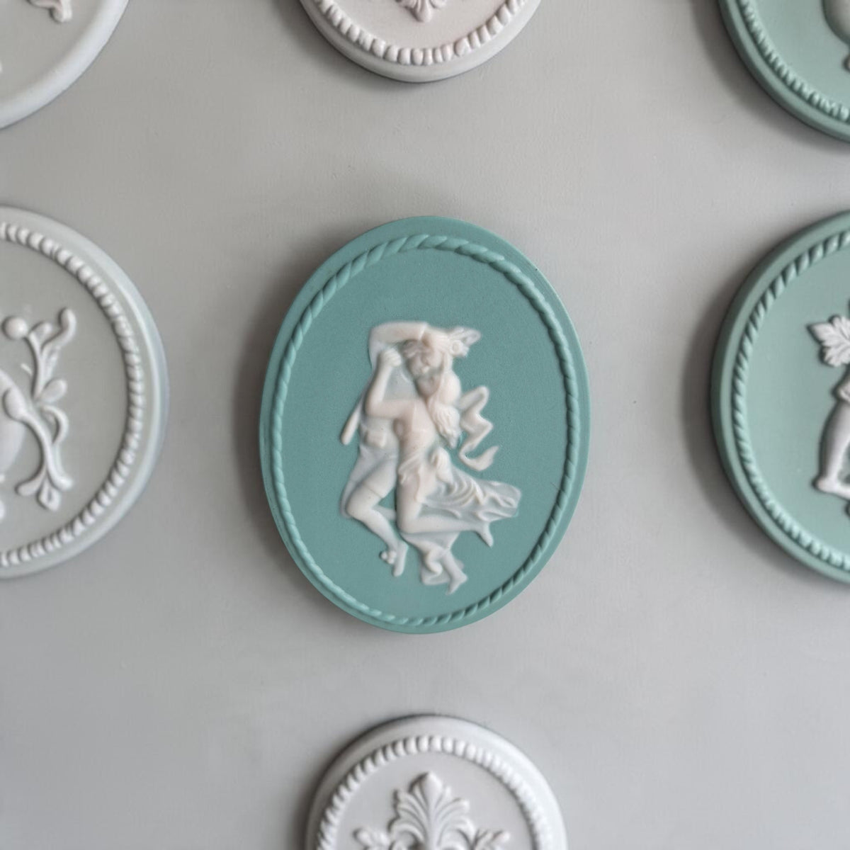 Ovaal zeegroen Villeroy & Boch Mettlach wandmédaillon met een wit reliëf van een omhelzend koppel en een decoratieve touwrand.