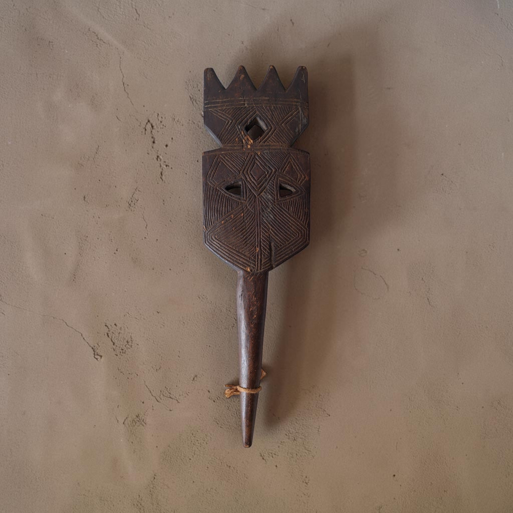 Handgesneden houten bedpoot uit Niger met geometrische inkervingen op een plat vlak, donker verweerd hout en een spitse grondpin.
