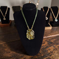 Handgemaakt bohemian collier met bronskleurige hanger en gevlochten groene koorden, totale lengte 51cm
