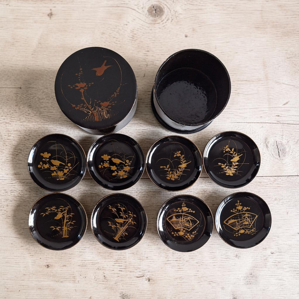 Vintage Japanse lakwerk onderzetterset met ronde opbergdoos, gouden maki-e motieven van vogels, bloesem, bamboe en waaiers, h5,5 x Ø9,3 cm.
